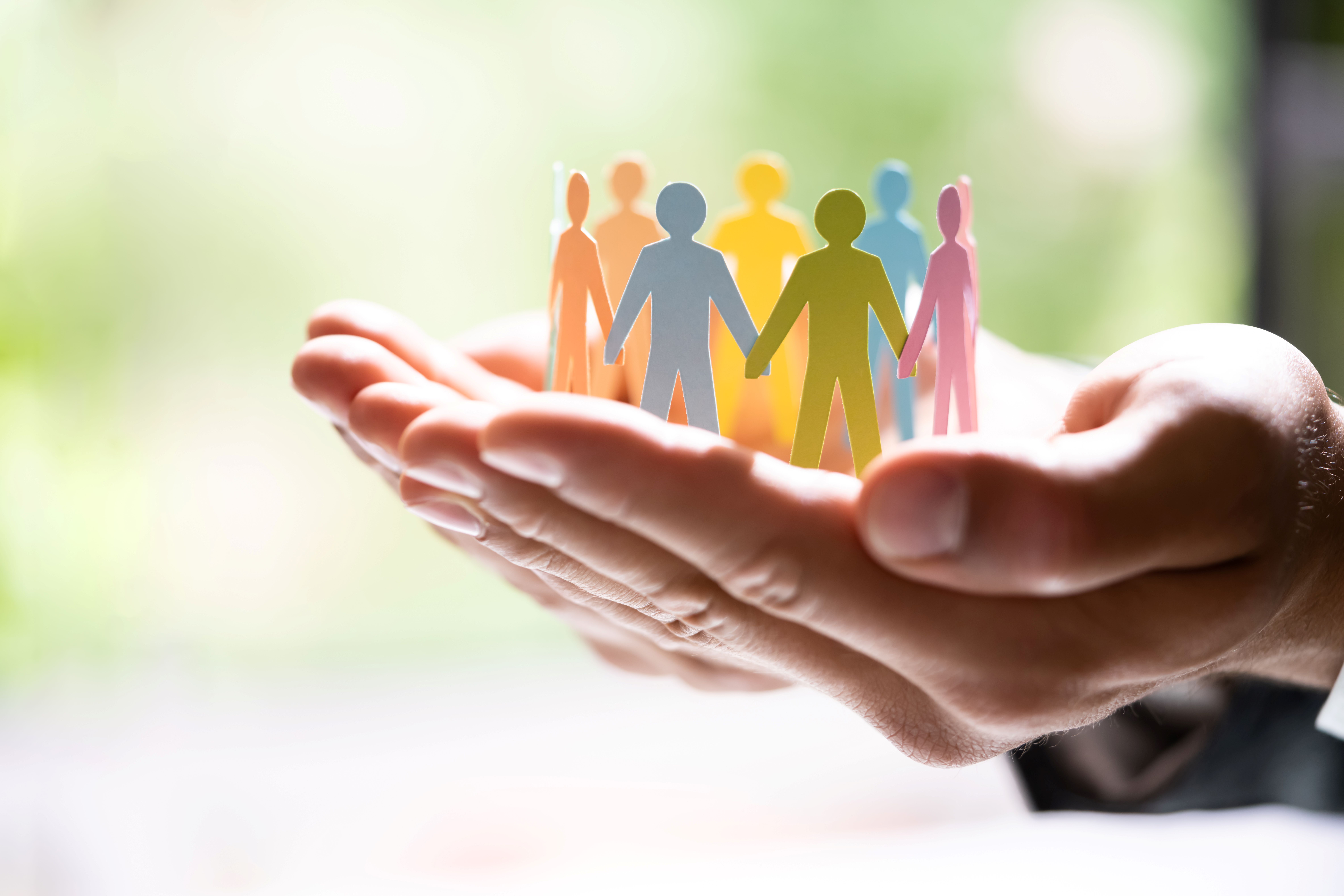 Cupped hands holding multi-color paper cutouts of people holding hands.